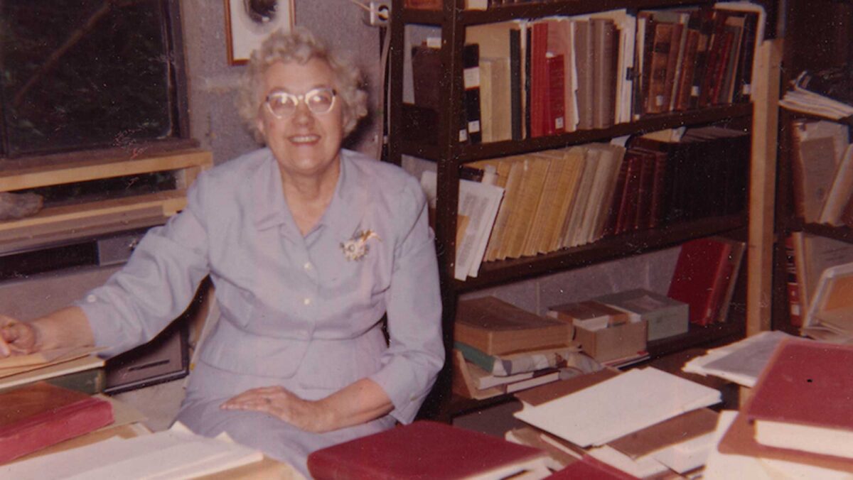Photograph of paleontologist Katherine Palmer behind a stack of books, circa 1960.